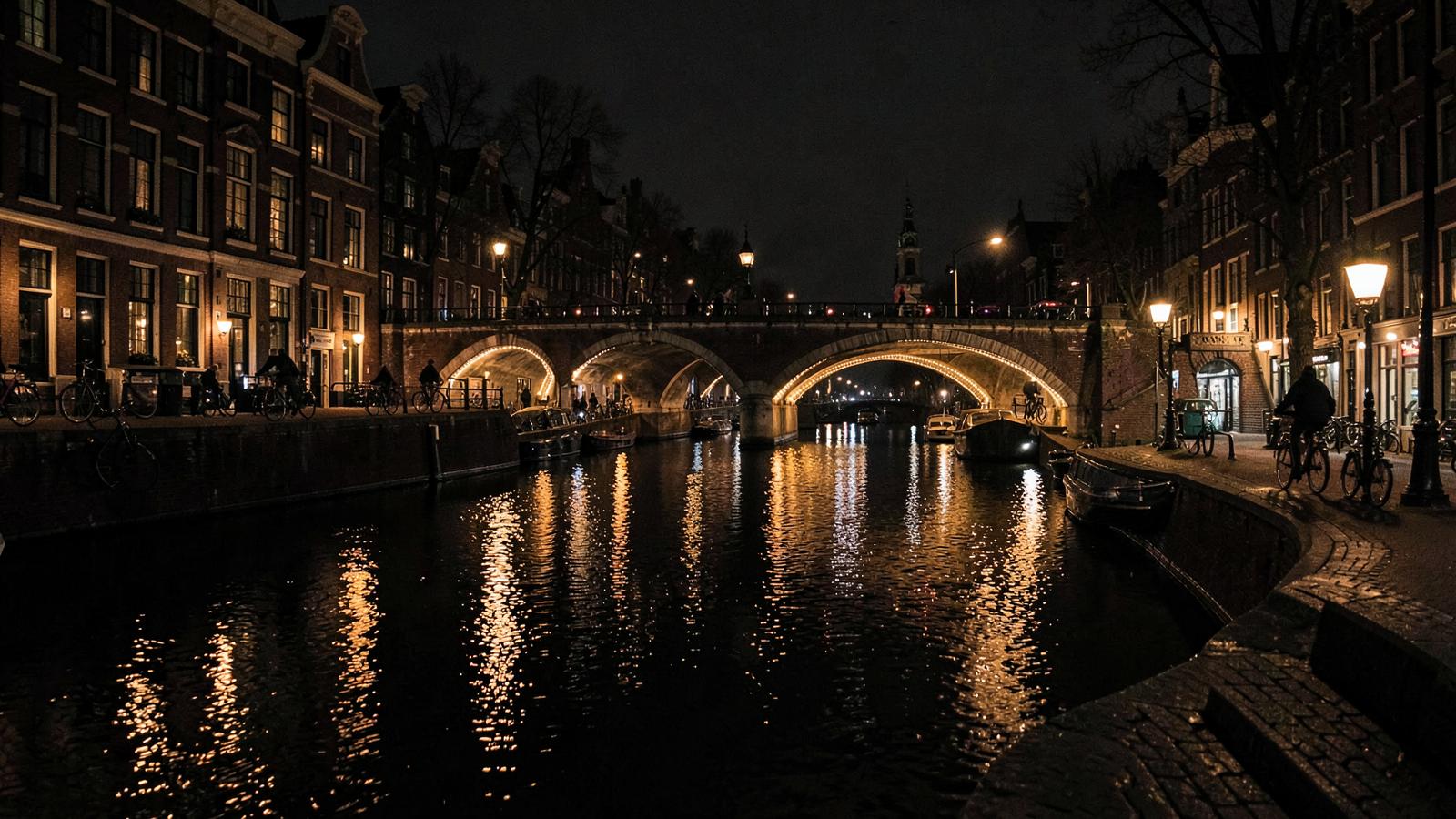 Canal houses reflected in the water along an Amsterdam canal lit by street lamps at night