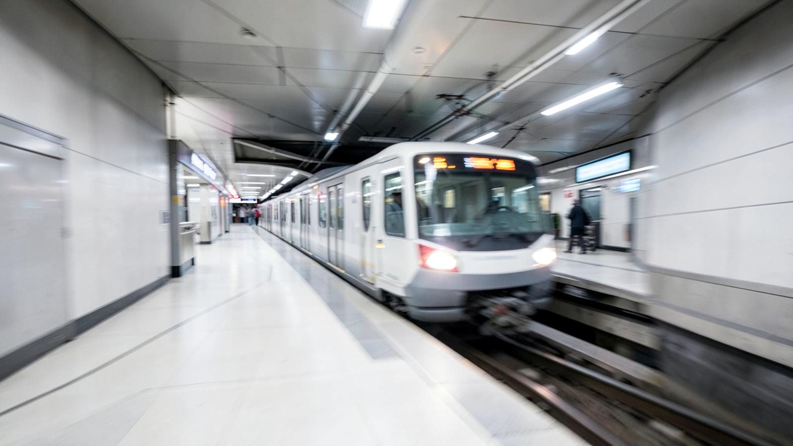 Passengers waiting on a platform at an Amsterdam metro station beside a yellow tap-in pole