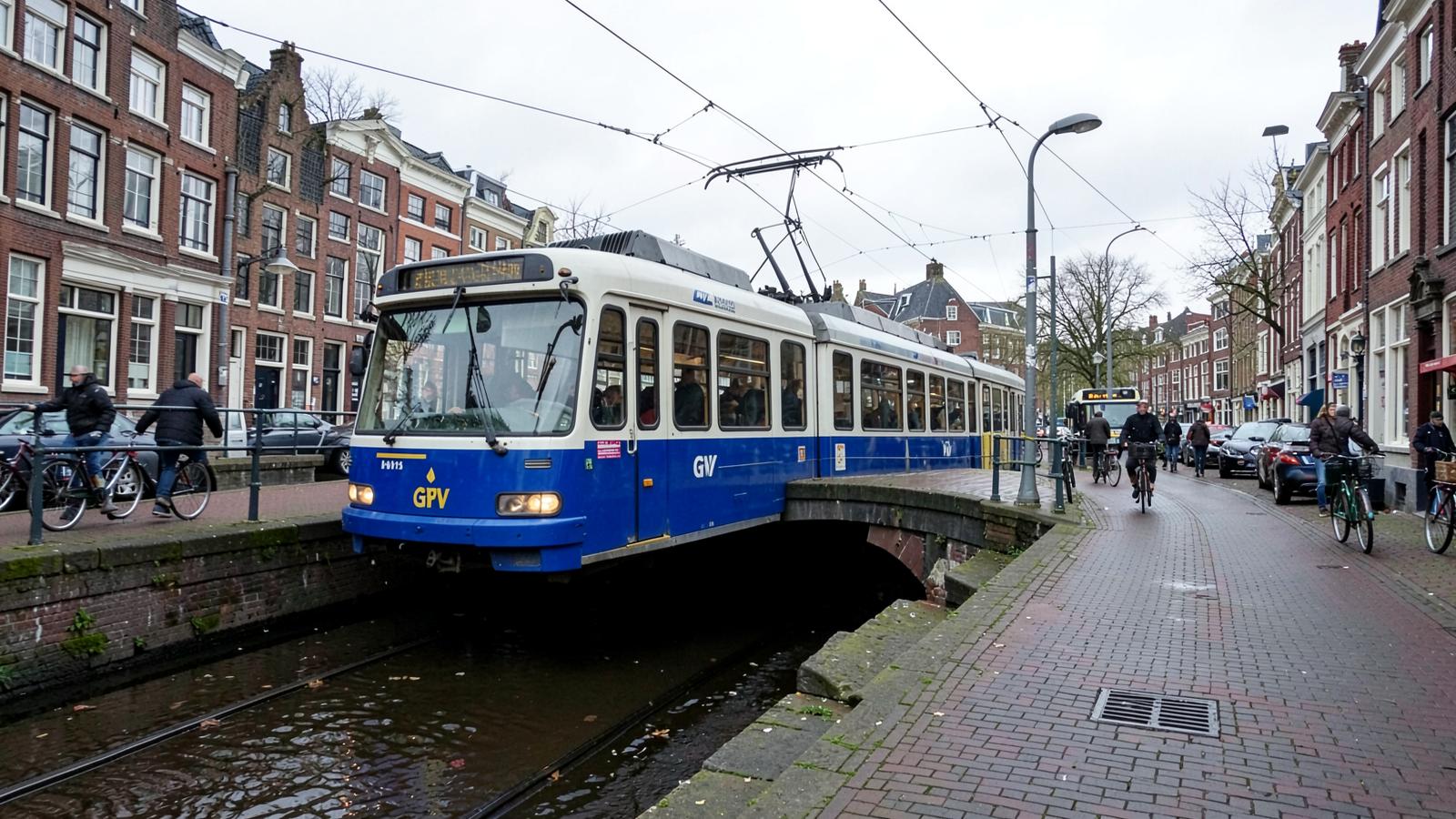A blue and white GVB tram travelling along an Amsterdam canal street